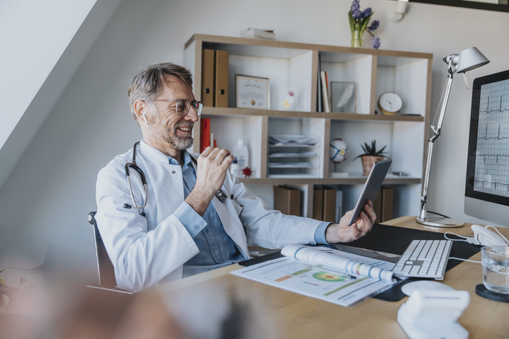 Mature vet talking on video call over digital tablet while sitting at doctor's office