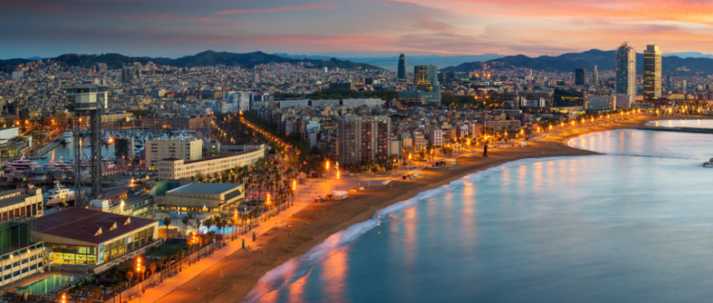 Aerial view of Barcelona with colorful streets and the Mediterranean Sea in the foreground.
