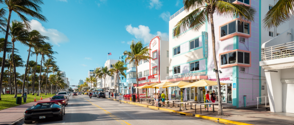 Vibrant South Beach street scene bustling with colorful art deco architecture, cafes, and palm-lined avenues under the warm afternoon sun.